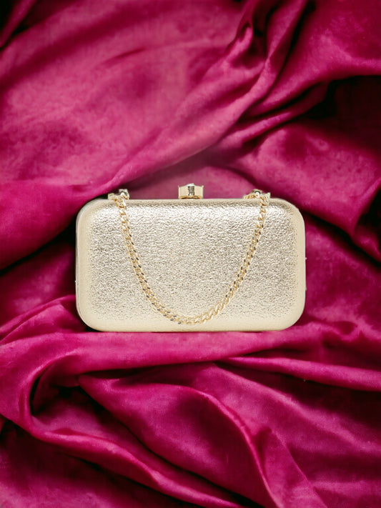 A Vdesi Base gold clutch with a metal chain on a pink velvet fabric.