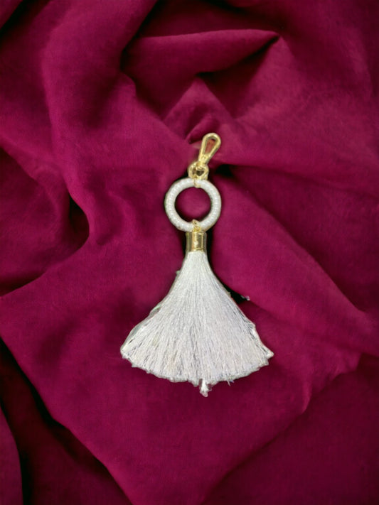 A Vdesi white tassel bag charm on a plain red sheet. 
