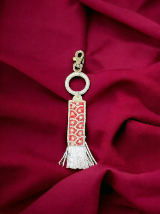 A Vdesi white & red tassel bag charm on a plain red sheet. 