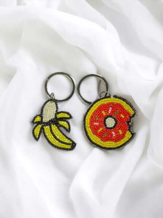 Two Vdesi keychains with a banana and a fruit on them, also serving as bag charms.